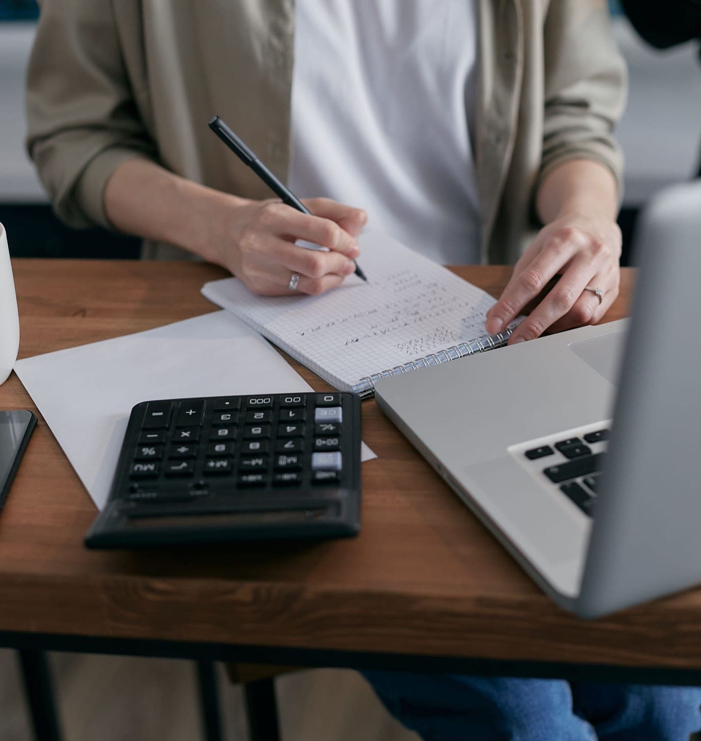 Profissional conferindo lançamentos financeiros no notebook, com calculadora e anotações sobre a mesa
